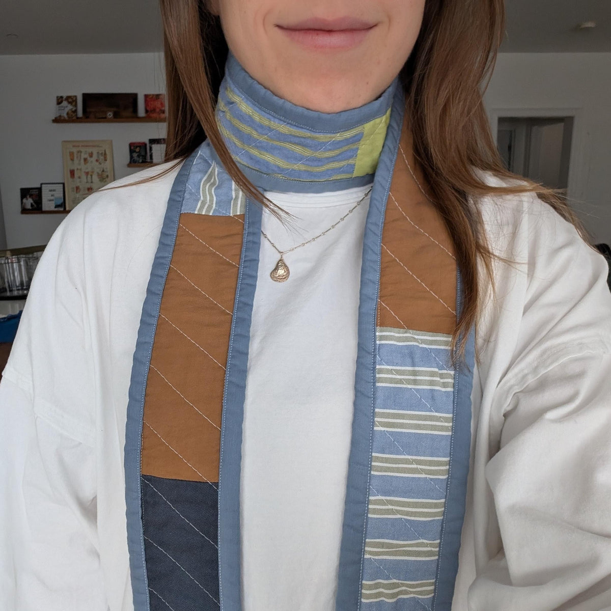 Close up of person wearing a quilted scarf with blue, green, white, and brown coloring. 