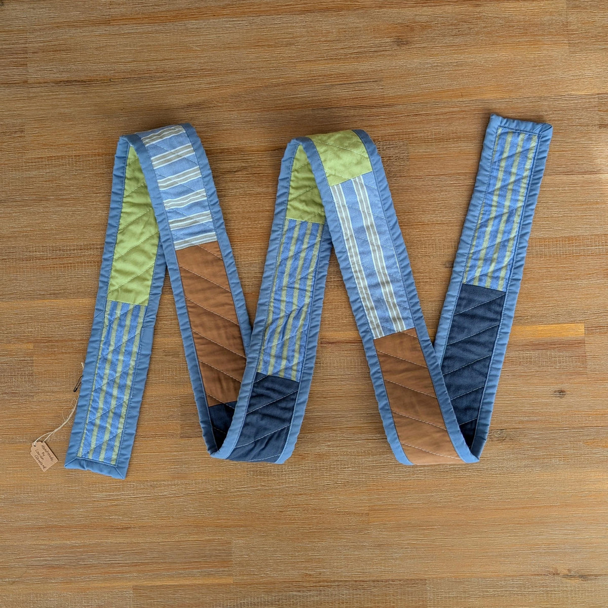 Handmade quilted scarf with blue binding laid on a wooden surface
