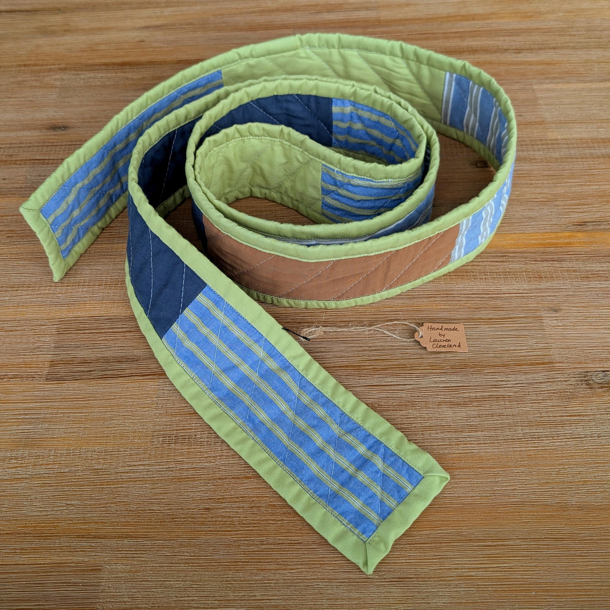 Handmade quilted scarf with green binding laid on a wooden surface