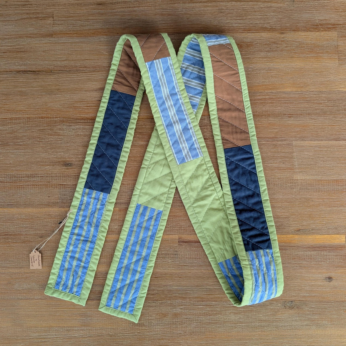 Handmade quilted scarf with green binding laid on a wooden surface