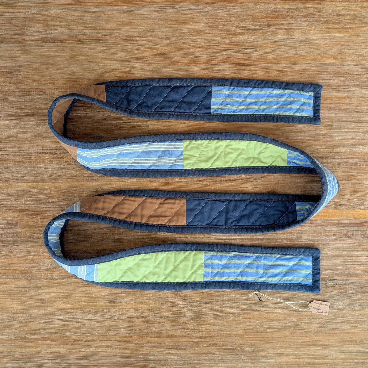 Handmade quilted scarf with navy binding laid on a wooden surface
